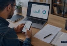 Pessoa utilizando uma plataforma fintech no celular e analisando informações financeiras no notebook.